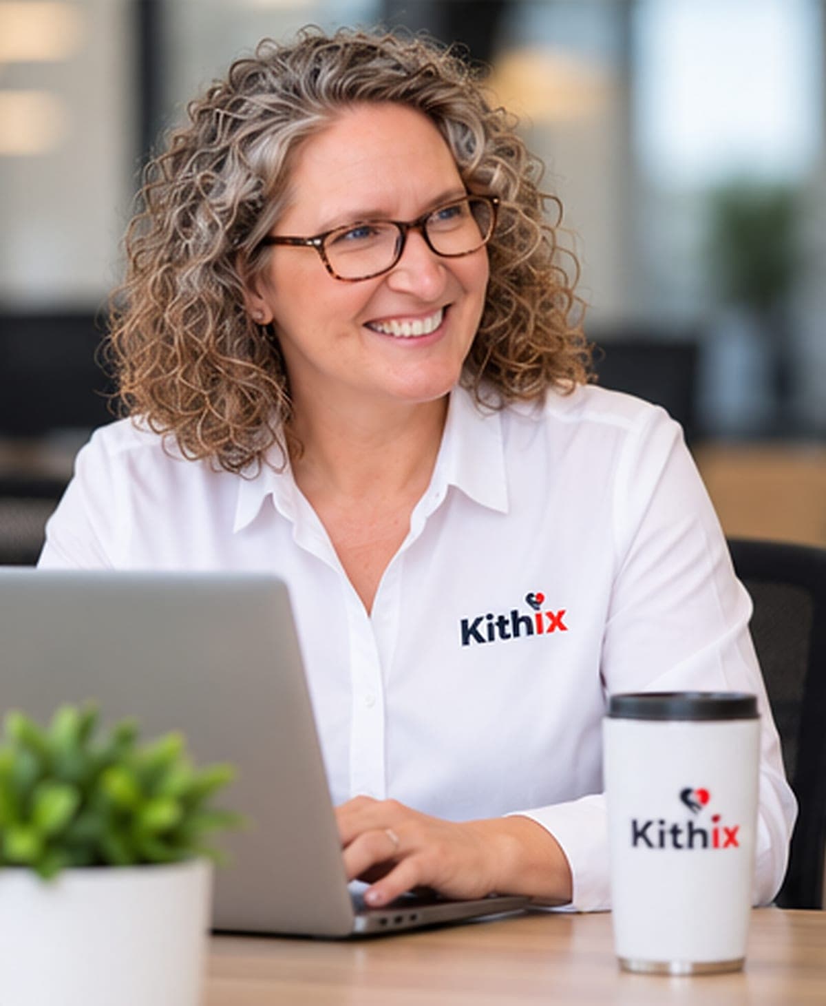 Amber Nash at a laptop in a white Kithix shirt, smiling, a Kithix cup beside her