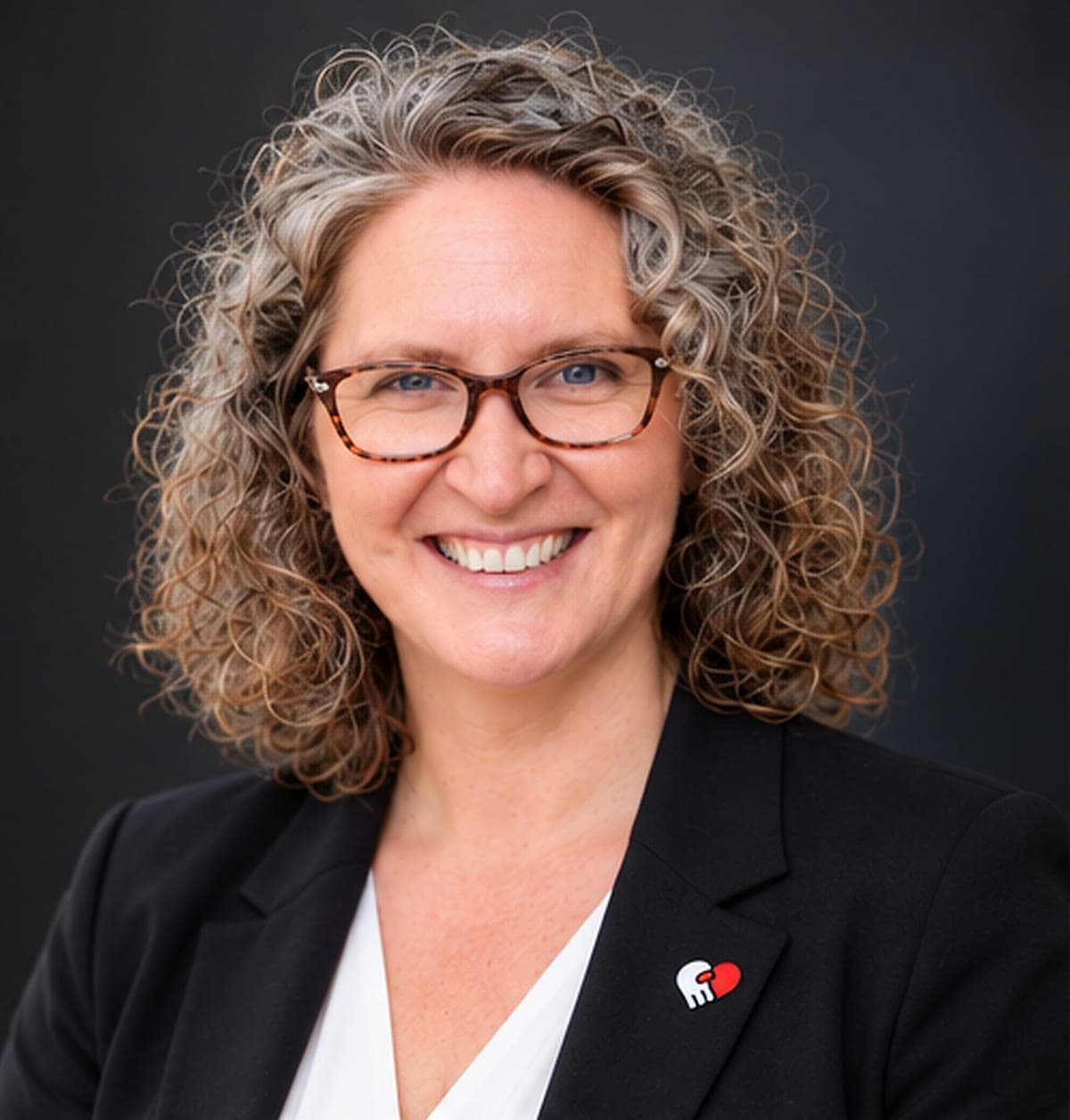 Amber Nash, the founder of Kithix, smiling, in a black blazer with a Kithix pin on the lapel